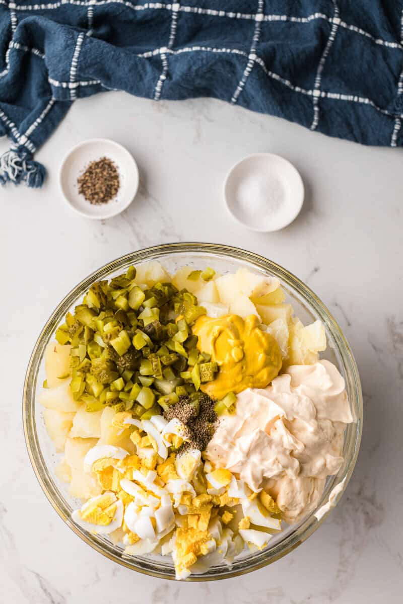mixing together all the ingredients for the potato salad in a large glass bowl.