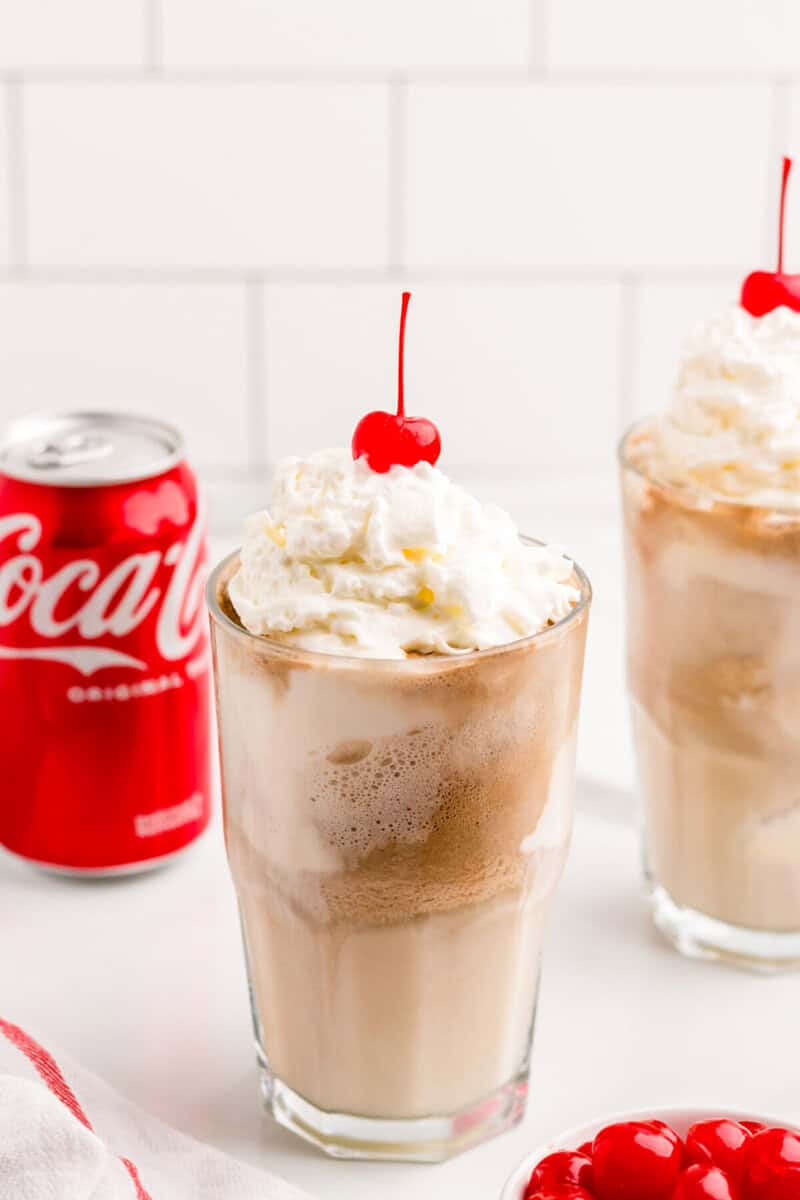 two Coke Floats topped with whipped cream and a cherry.