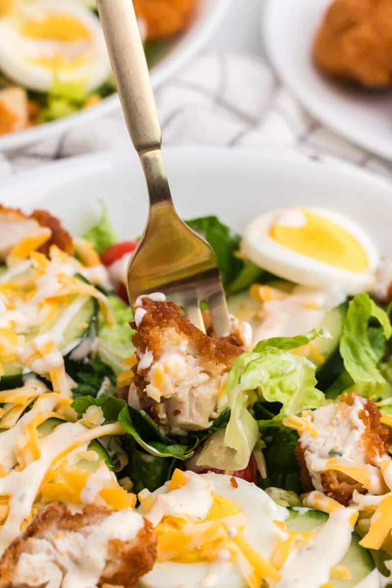 using a fork to take a bite of the crispy chicken salad.