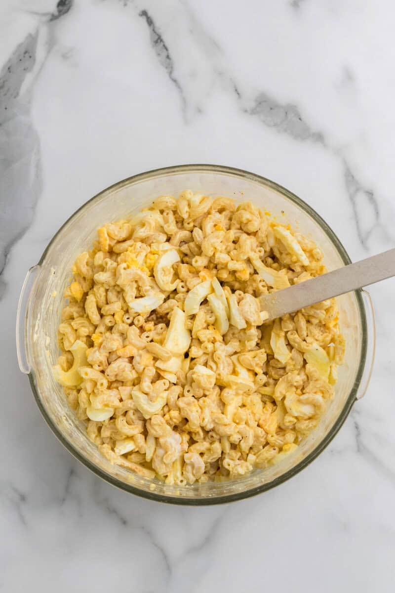 folding in the sliced hard-boiled eggs into the pasta salad.