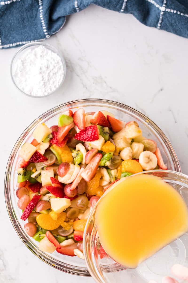 pouring the vanilla orange juice dressing over the fruit salad.