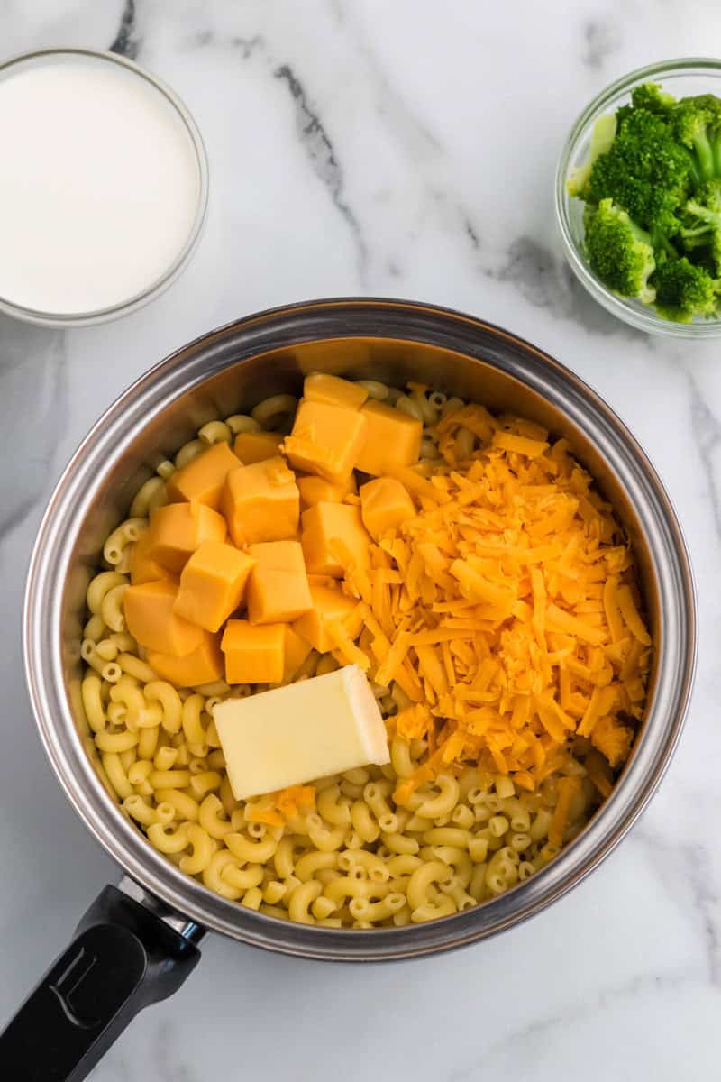 adding the butter and cheeses to the noodles in the pot.