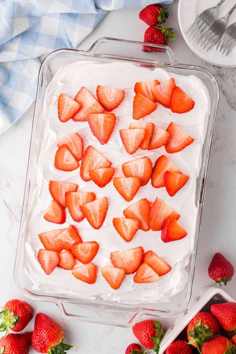 topping the cake with sliced strawberries.