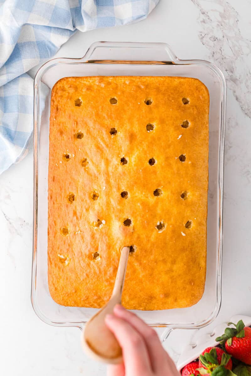 using a wooden spoon to poke holes into the cake.