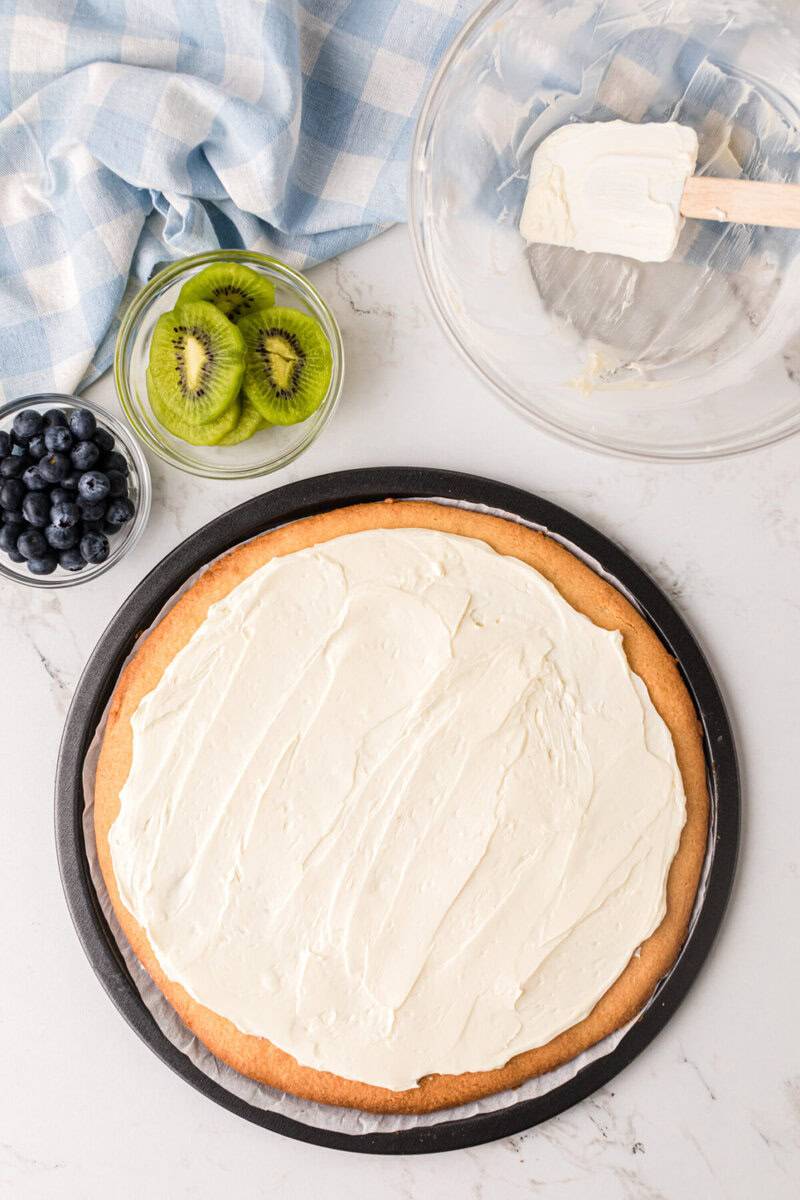 spreading the cream cheese sauce on the cookie pizza.