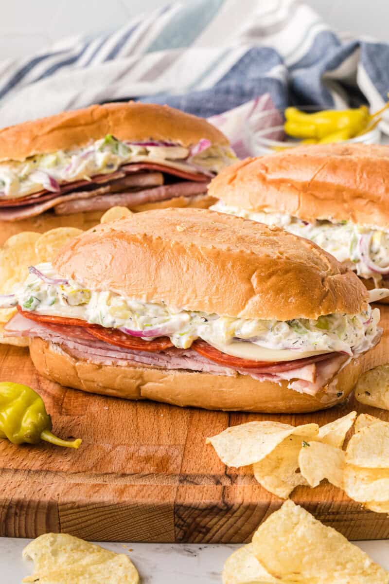 three grinder sandwiches served on a wooden board.