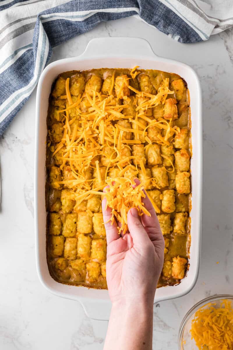 adding shredded cheese to the top of the casserole.
