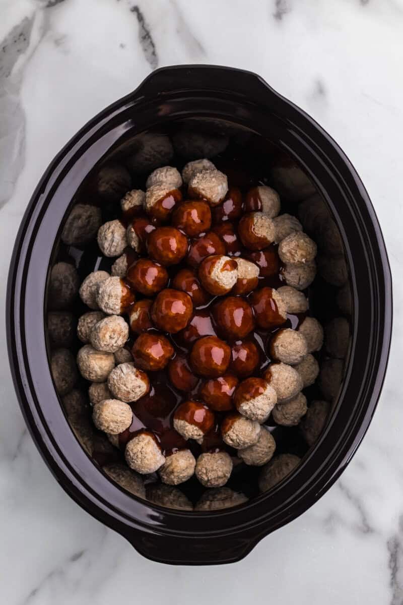 pouring the BBQ sauce on top of the meatballs in the slow cooker.