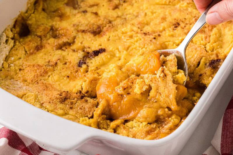 Peach Dump Cake in white baking dish being served with a metal spoon.