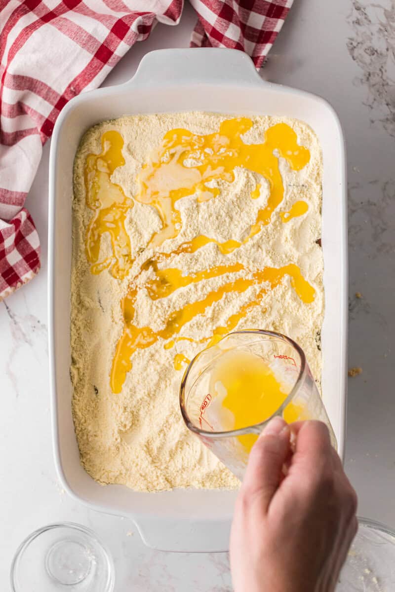 pouring the melted butter on top of the cake mix in the baking dish.
