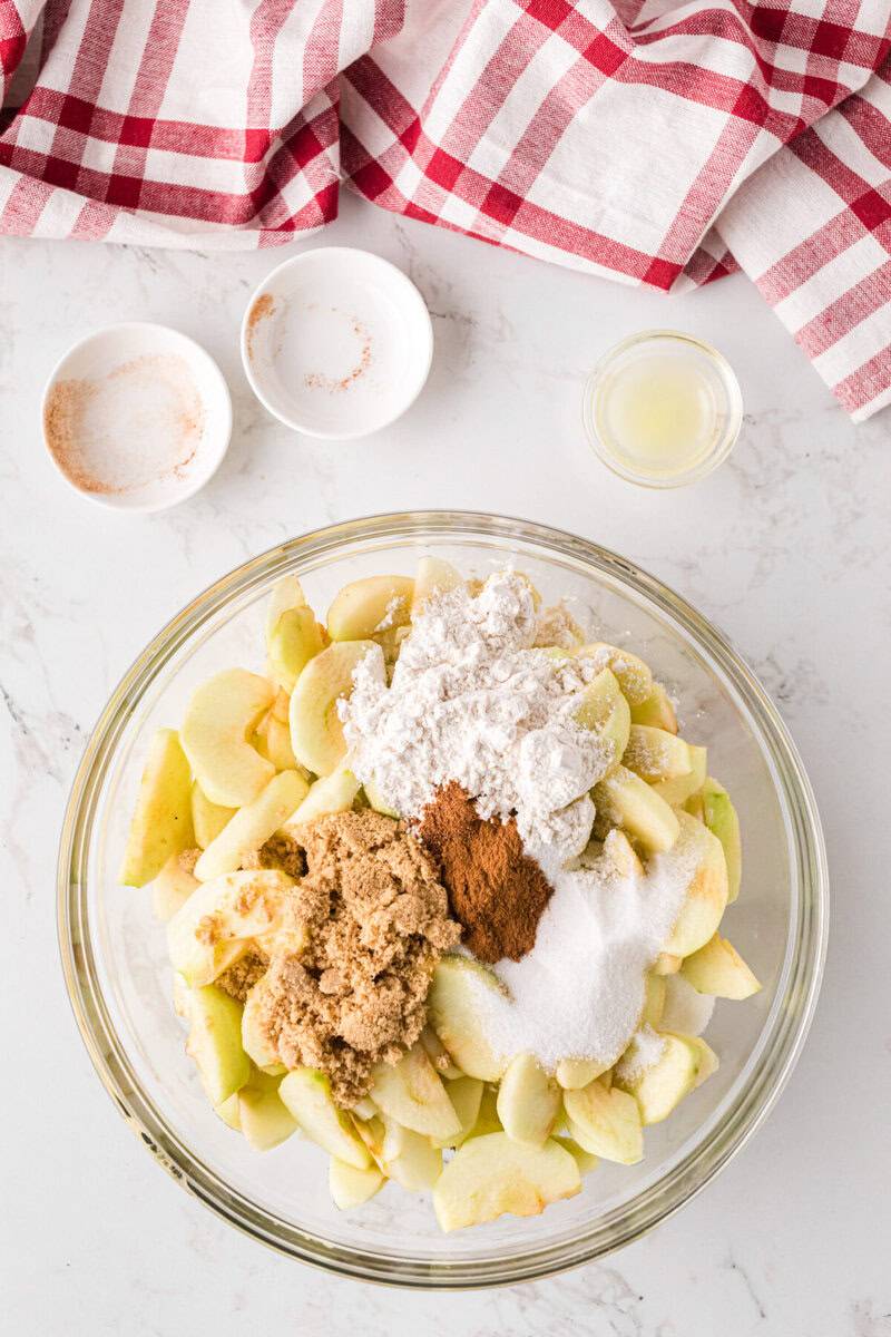 apple slices with sugars, flour and cinnamon in a large glass mixing bowl.