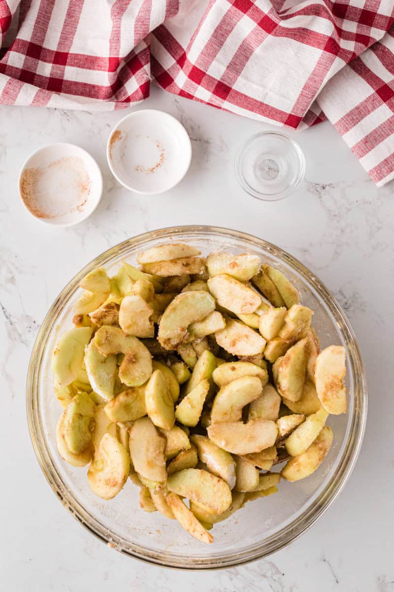 apples mixed in the cinnamon sugar in the glass bowl.