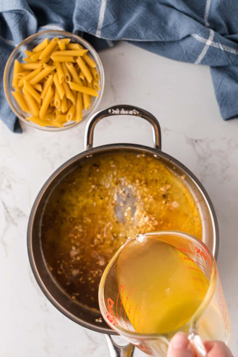 pouring the broth into the skillet with the cooked garlic.