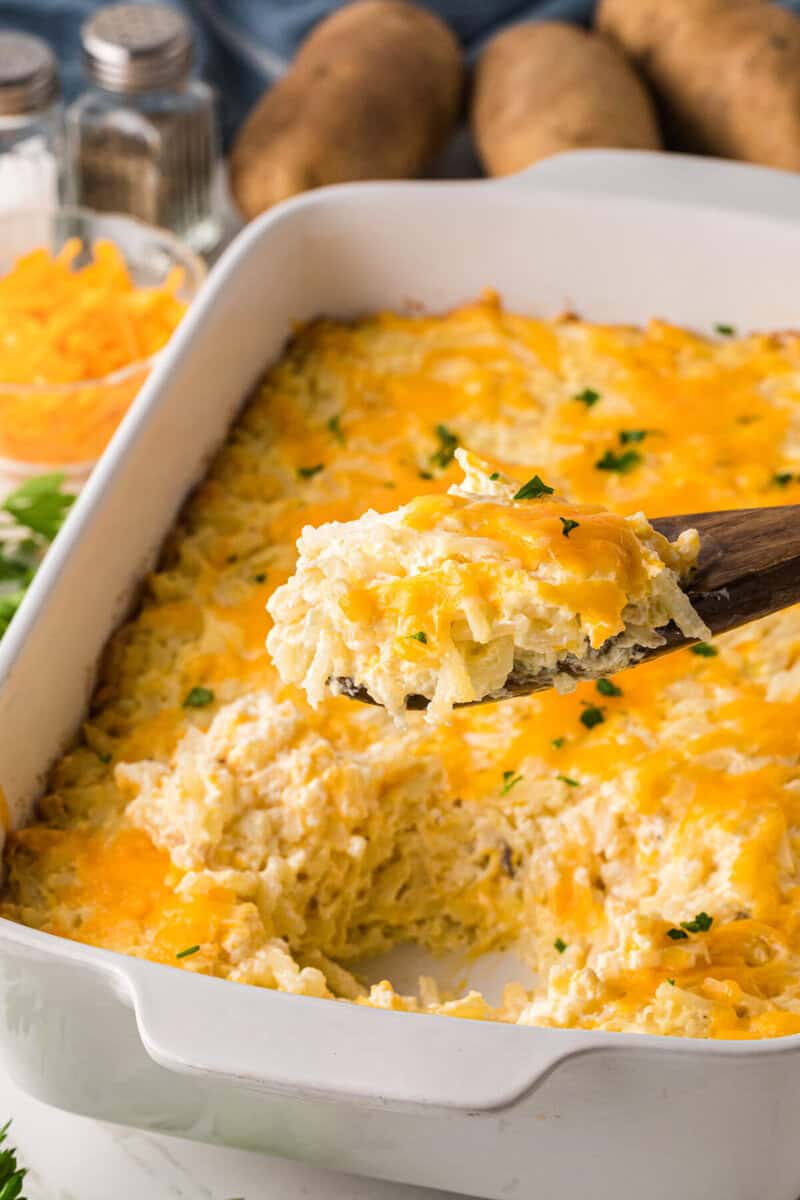 serving the hashbrown casserole out of the casserole dish with a wooden spoon.