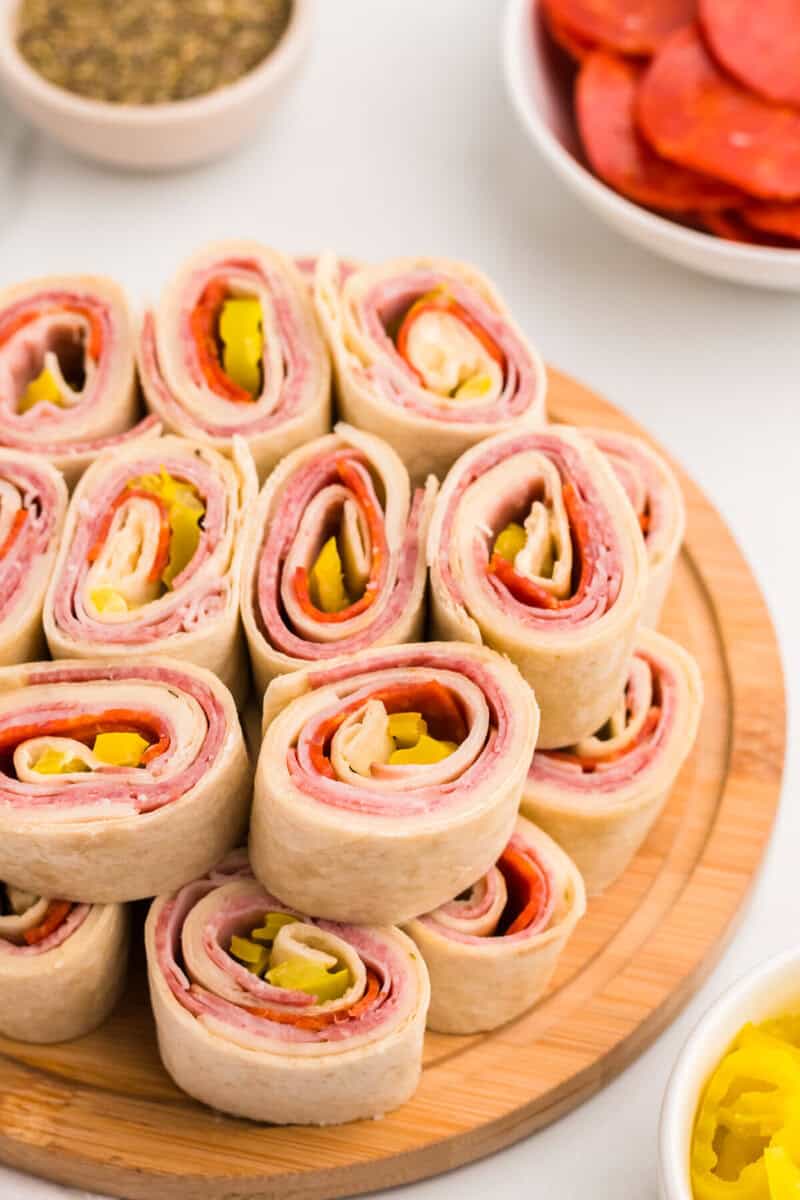 Italian Pinwheels stacked on top of each other on a wooden serving board.