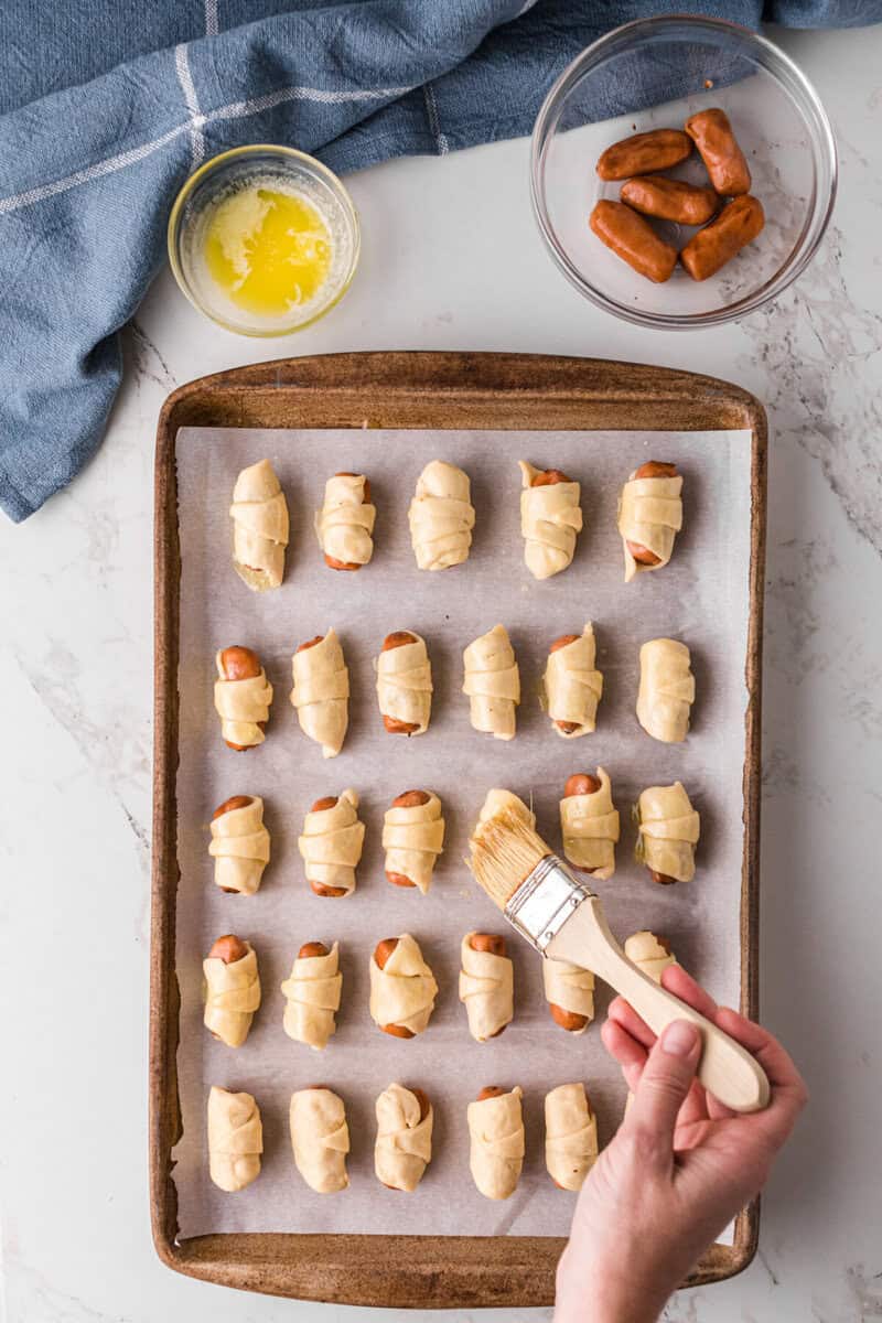 brushing the Pigs in a Blanket with melted butter.