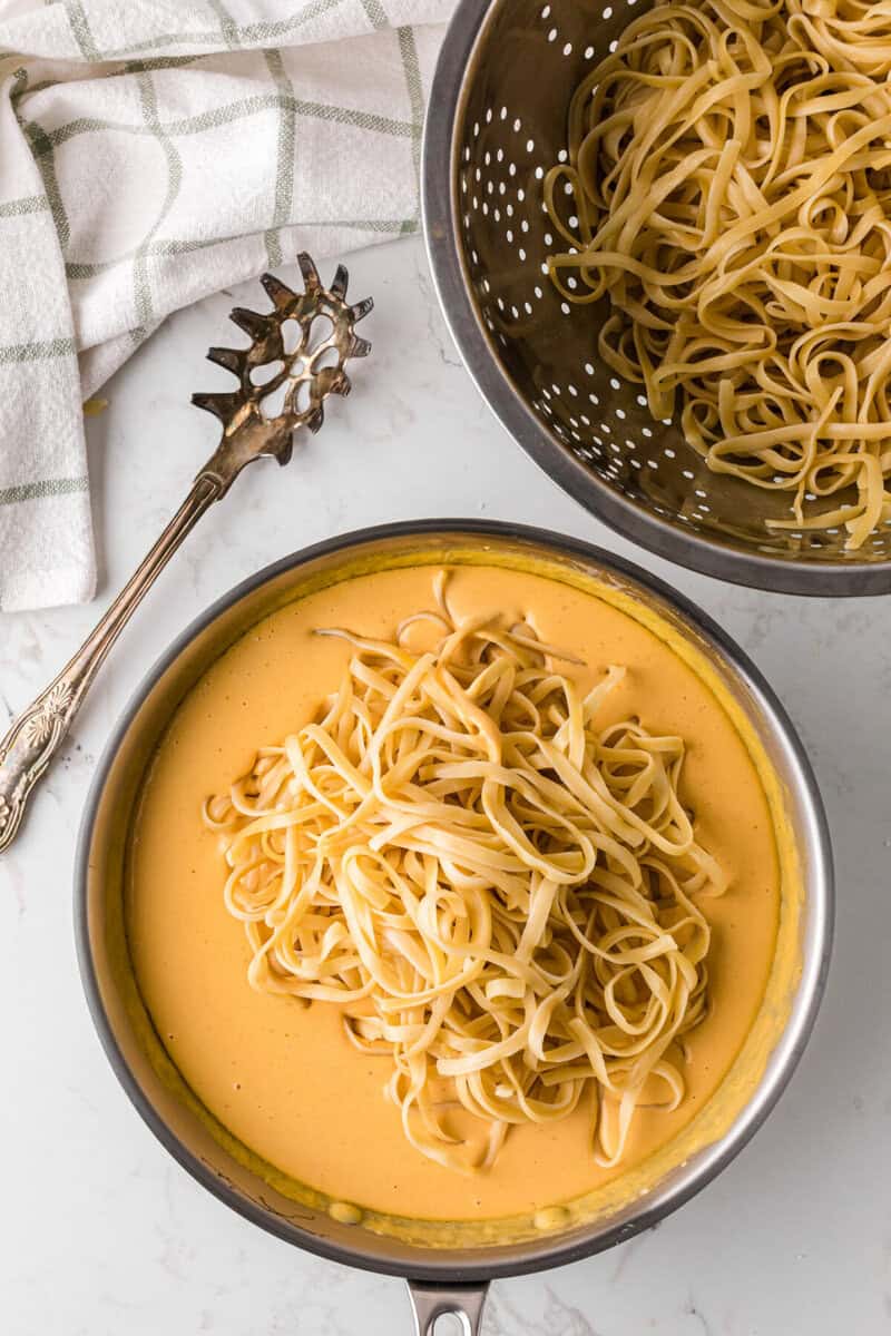 adding the pasta to the pumpkin alfredo sauce.