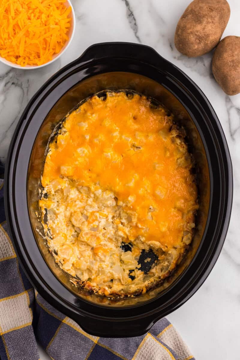 Cheesy Potato Casserole in the slow cooker with a serving scooped out.