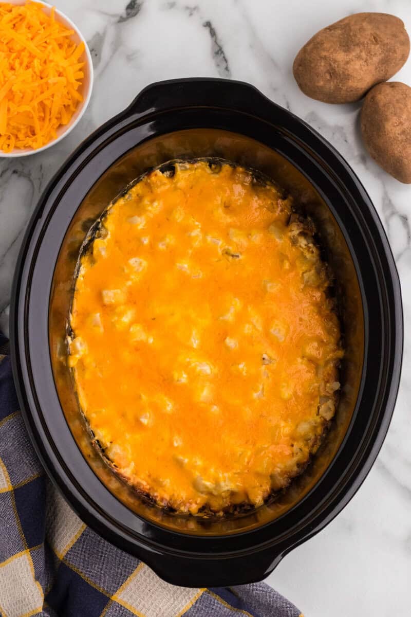 finished Cheesy Potato Casserole in the slow cooker topped with cheddar cheese.