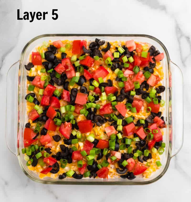 top-down view of layer 5, the veggie layer, olives, tomatoes, and green onions.