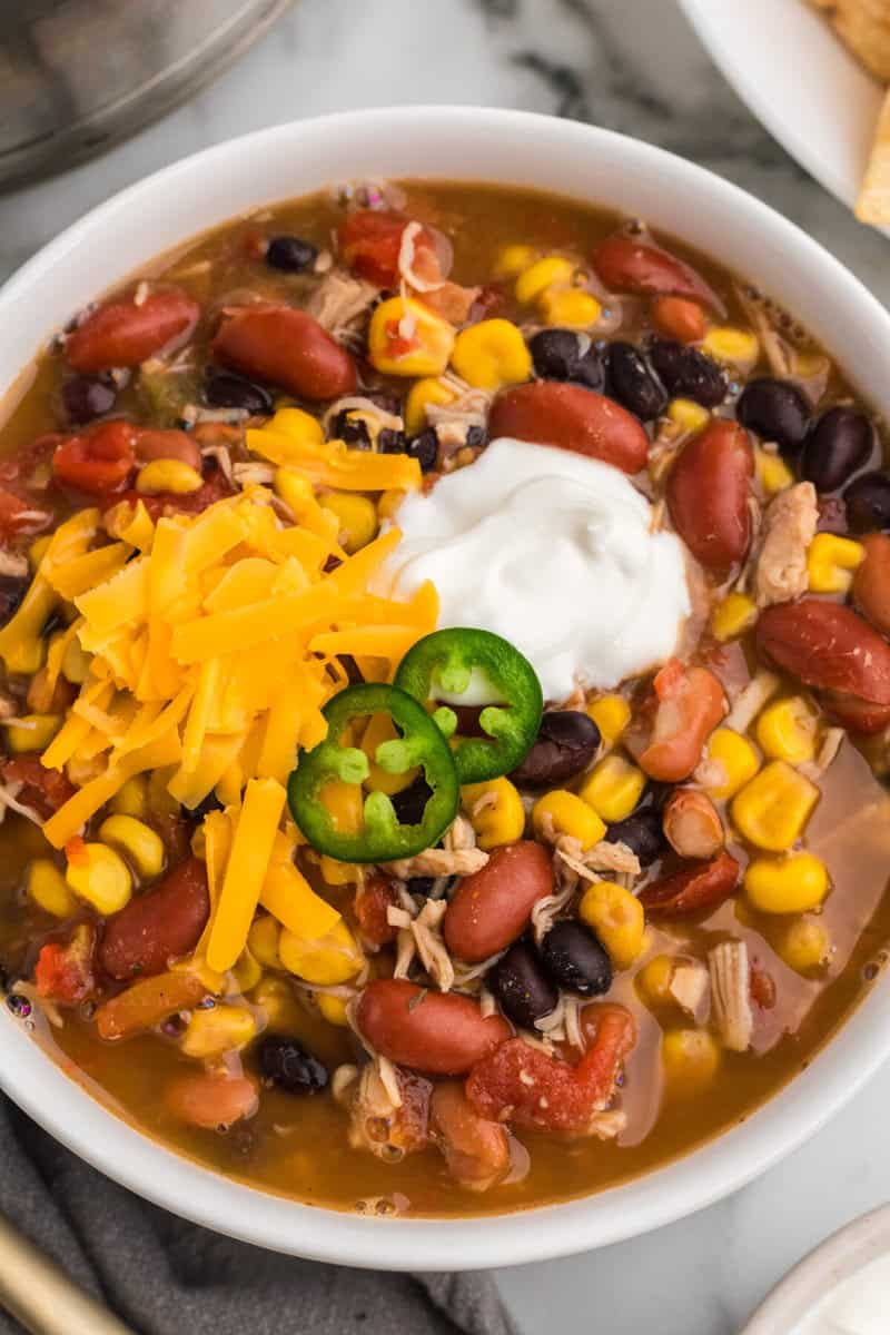closeup of the taco soup served in a white bowl topped with cheddar cheese and sour cream.