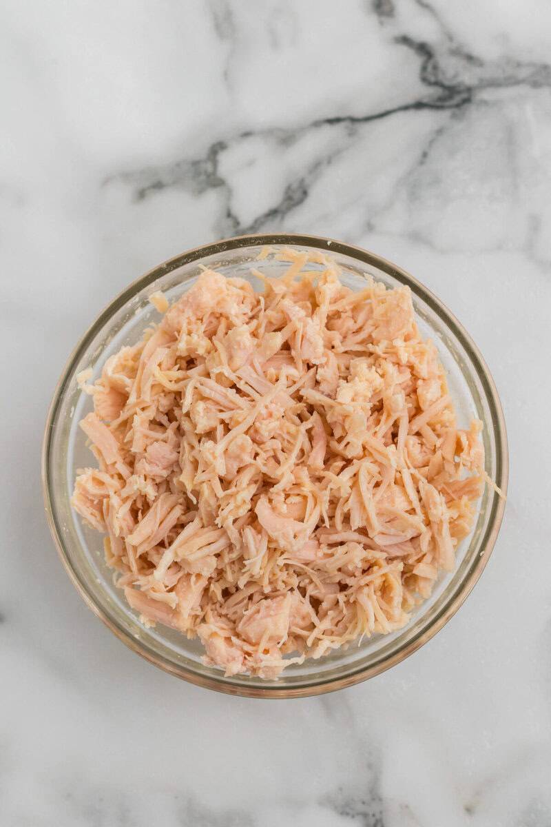canned chicken drained and shredded in a clear glass bowl.