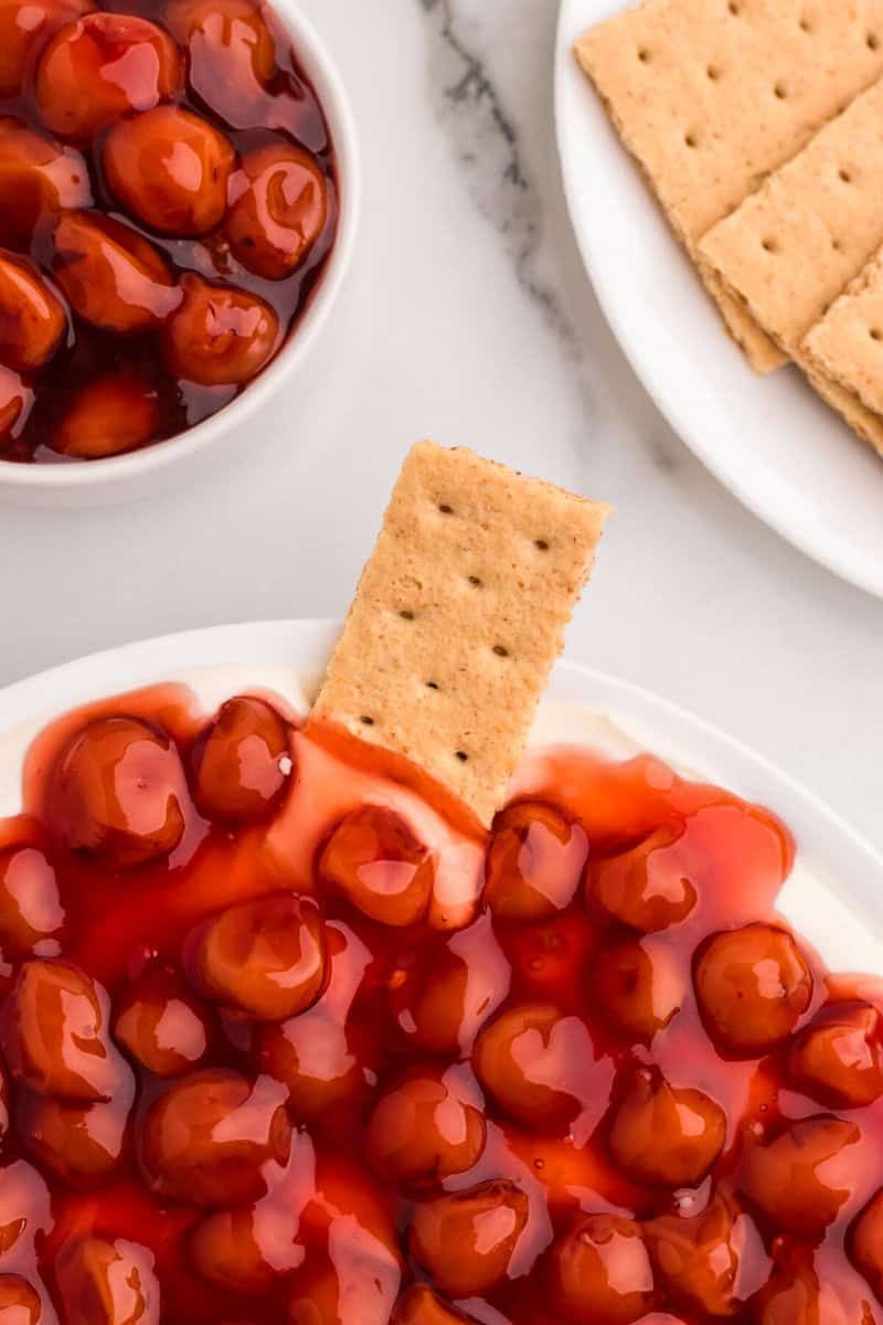 dipping a graham cracker into the Cherry Cheesecake Dip.