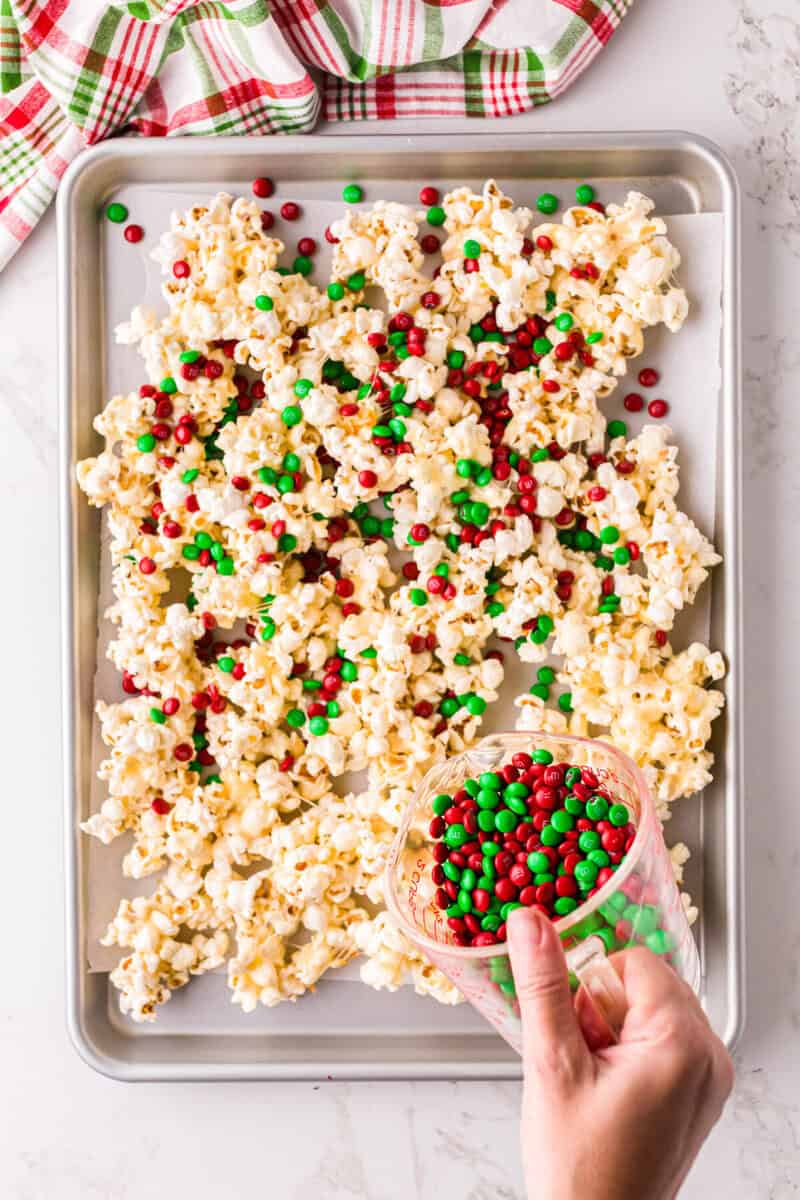 pouring the Christmas M&Ms over the popcorn.