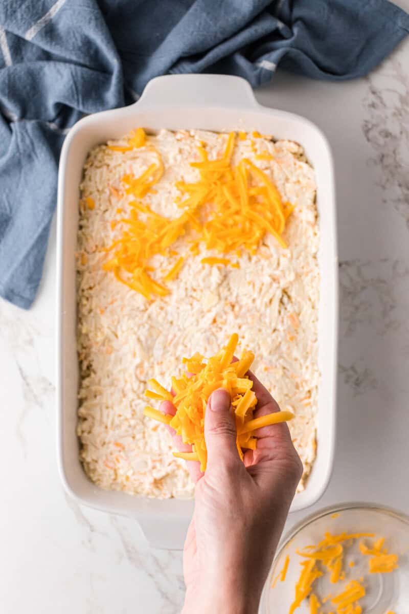 sprinkling cheese on top of the hashbrown casserole in the baking dish.