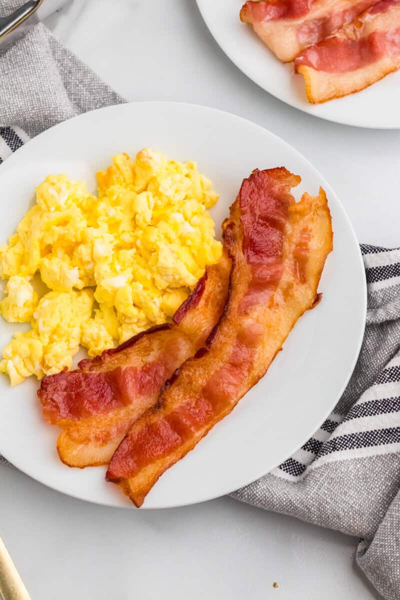 two slices of bacon on a plate with eggs.