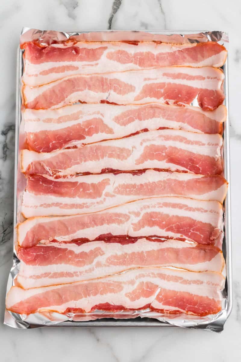 raw bacon laid out on the baking sheet.