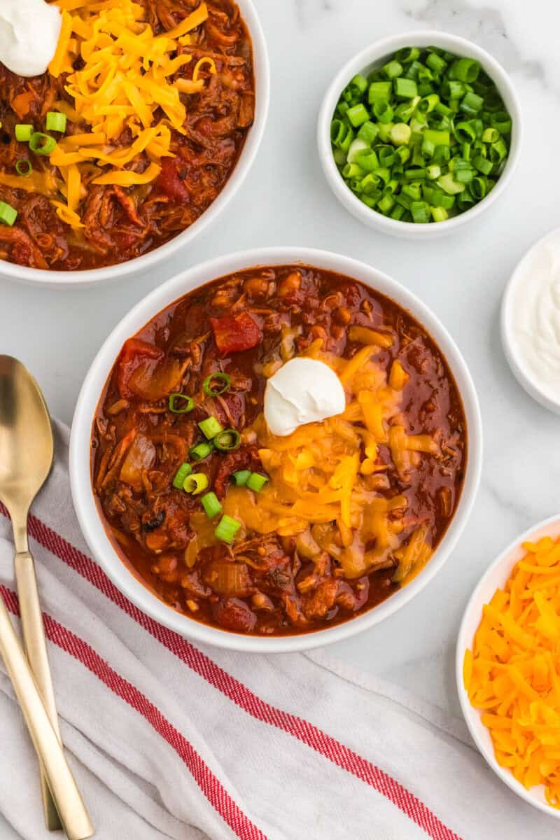 top-down view of the Pulled Pork Chili served in a white bowl topped with sour cream and cheese.