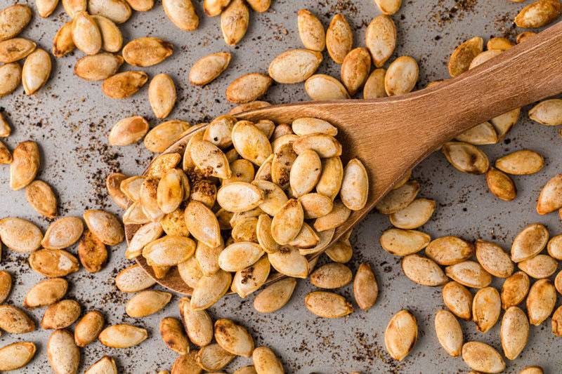 roasted pumpkin seeds being scooped with a wooden spoon.