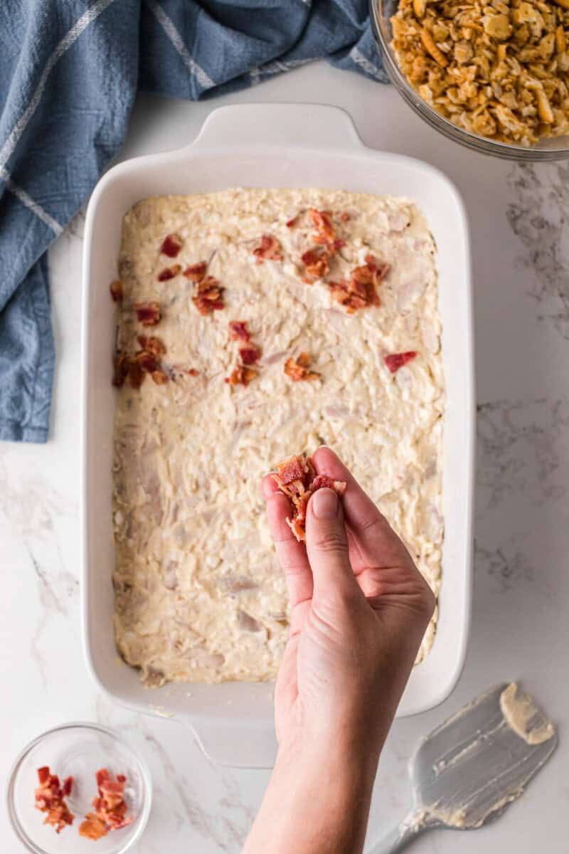 Million Dollar Casserole spread in casserole dish, being topped with bacon.