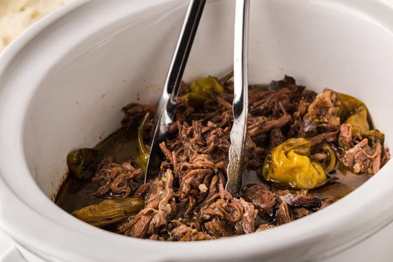 Slow Cooker Mississippi Pot Roast being served with tongs out of the slow cooker.