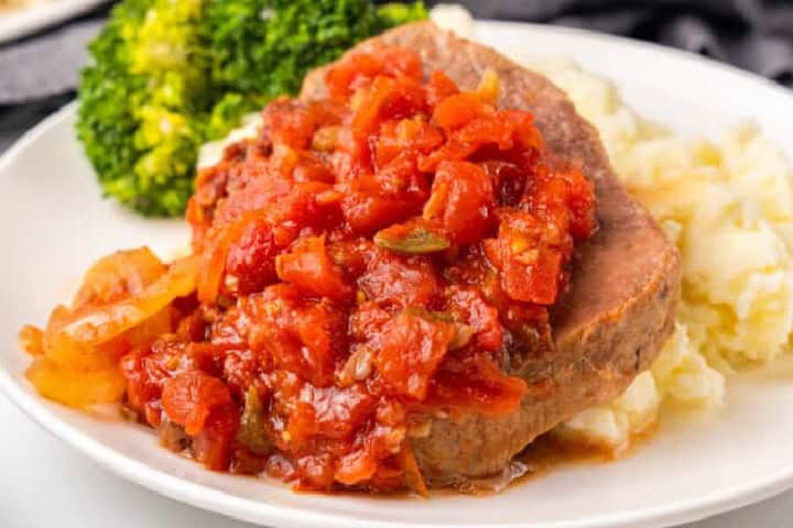 Slow Cooker Swiss Steak served on a plate with mashed potatoes and broccoli.