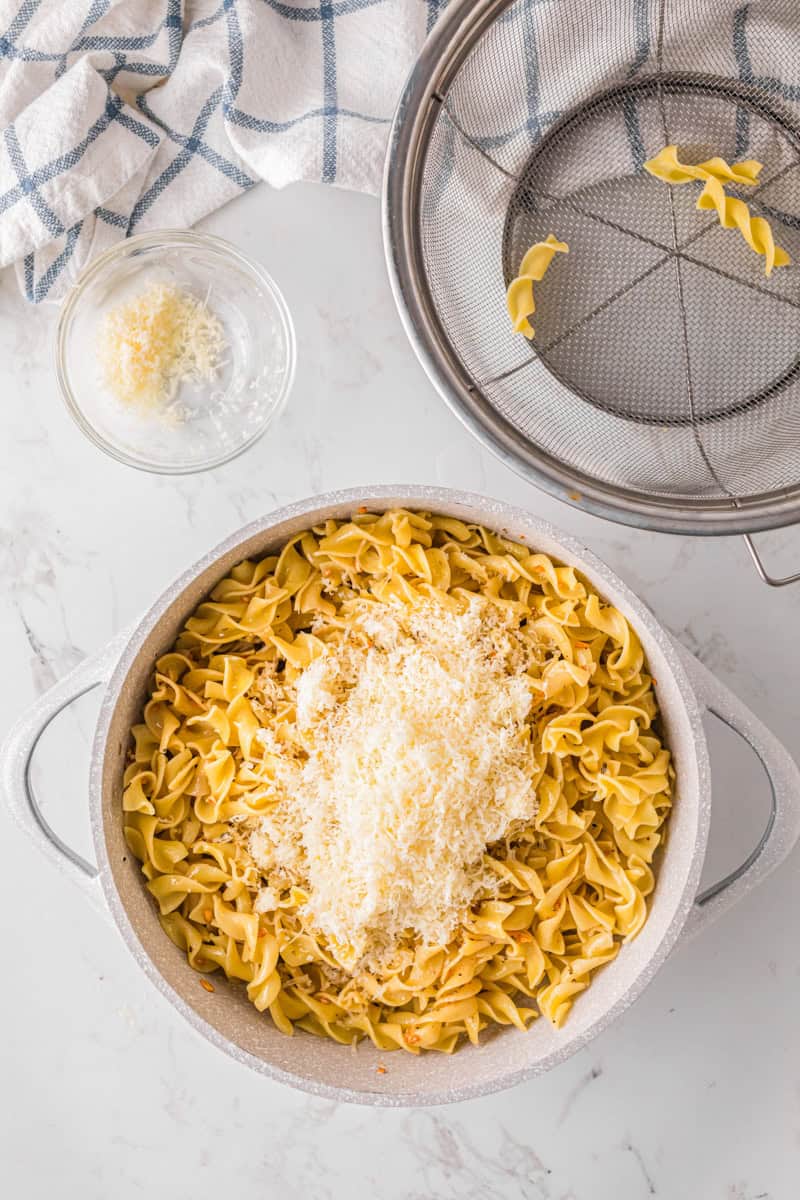 adding the cooked noodles and parmesan cheese to the butter and garlic. in the pot.