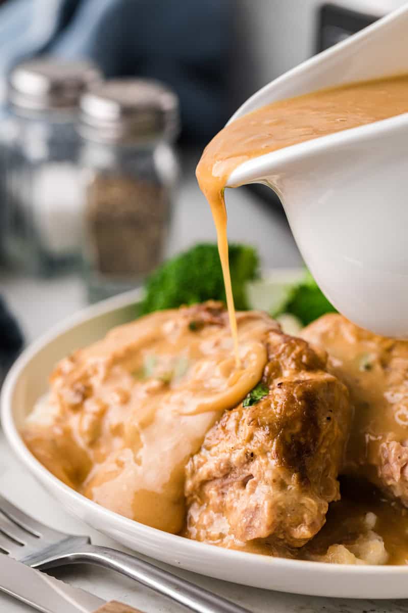pouring additional gravy on top of the plated pork chops.