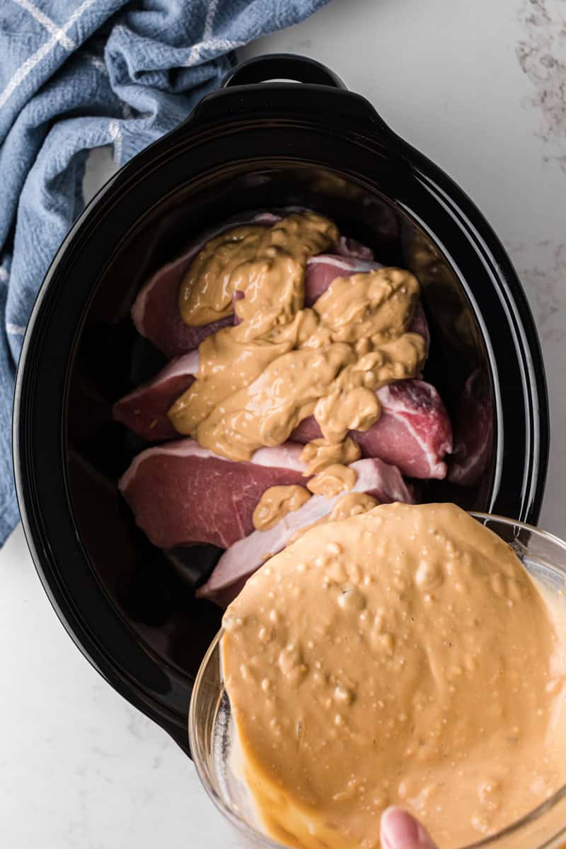 pouring the smother gravy over the pork chops in the slow cooker.