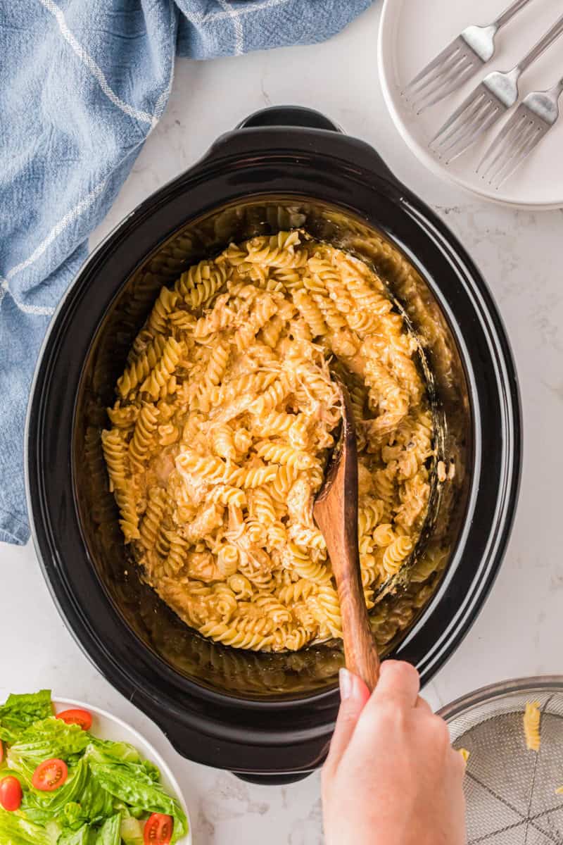 stirring in the rotini pasta to the chicken in the slow cooker.