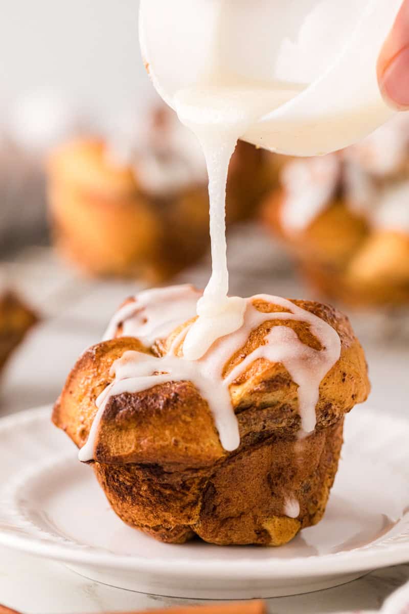 drizzling the frosting over the cinnamon roll muffin.