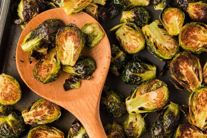 Roasted Brussel Sprouts served with a wooden ladle off the baking sheet.