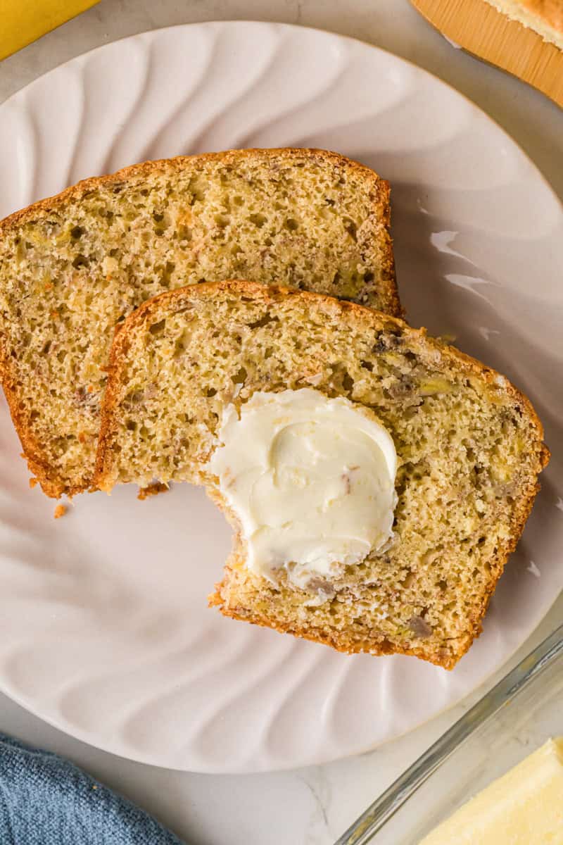 two slices of the Banana Bread served on a white plate with butter.