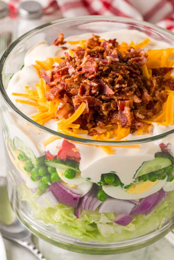 Delicious layered salad with chicken, bacon, avi, cheese, and fresh vegetables in a glass bowl. Perfect for summer meals or potlucks.