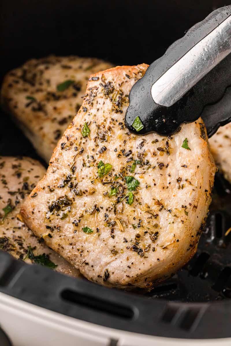 grabbing the pork chops out of the pan with tongs.