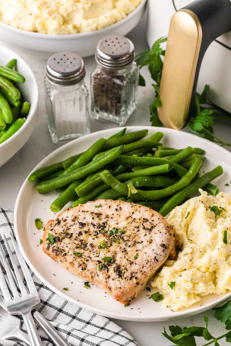 Air Fryer Pork Chops served on a white plate with mashed potatoes and green beans.