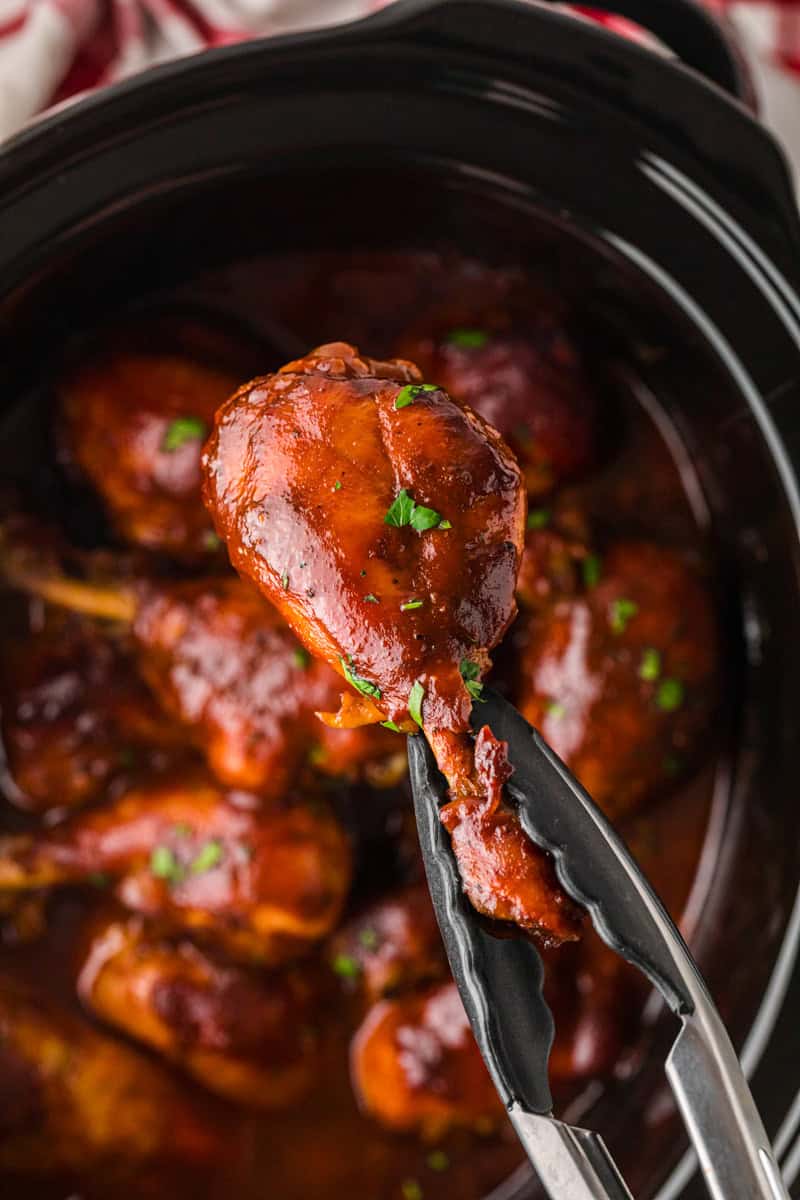 closeup of holding a BBQ Chicken Leg with tongs.