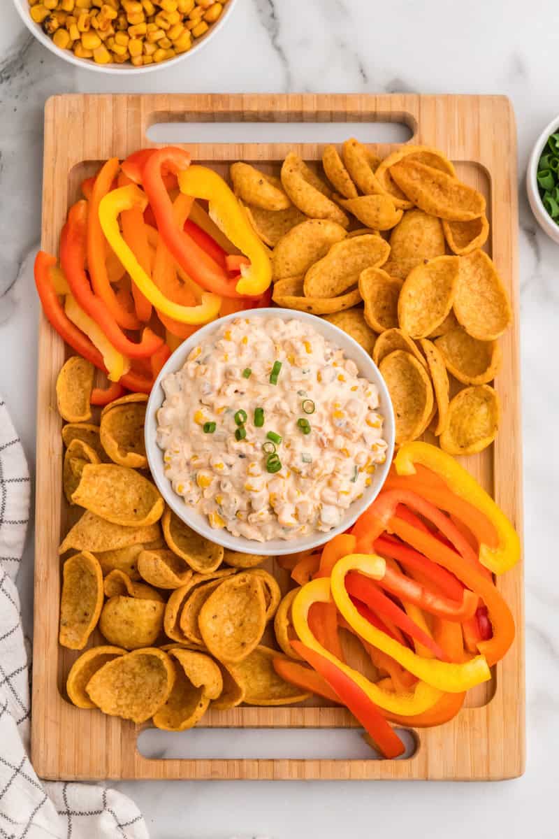 top-down view of the dip served on a wooden tray with peppers and chips.