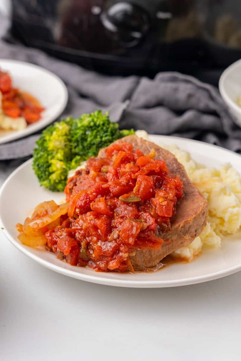 Swiss Steak served on a white plate on a bed of mashed potatoes.