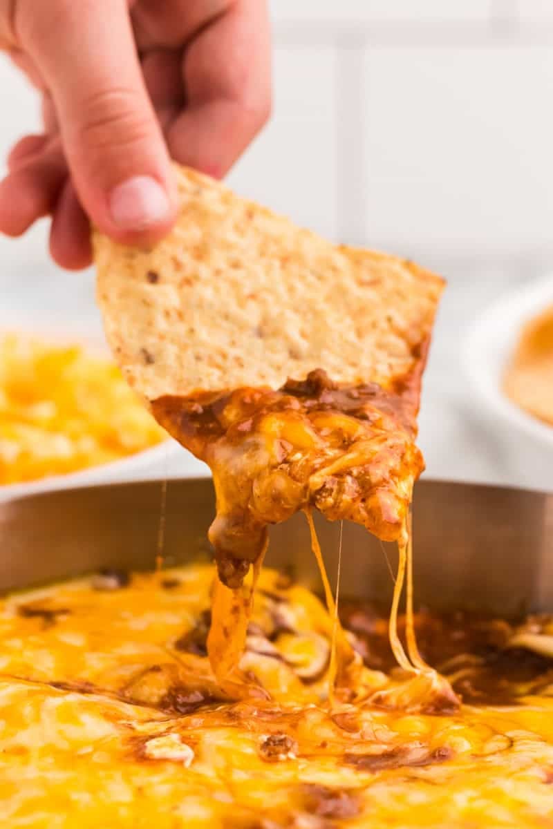 dipping a tortilla chip in the Chili Cheese Dip.